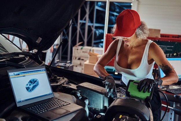 Une femme virile concentrée fait un diagnostic de voiture avec l'aide d'un ordinateur au service automobile.